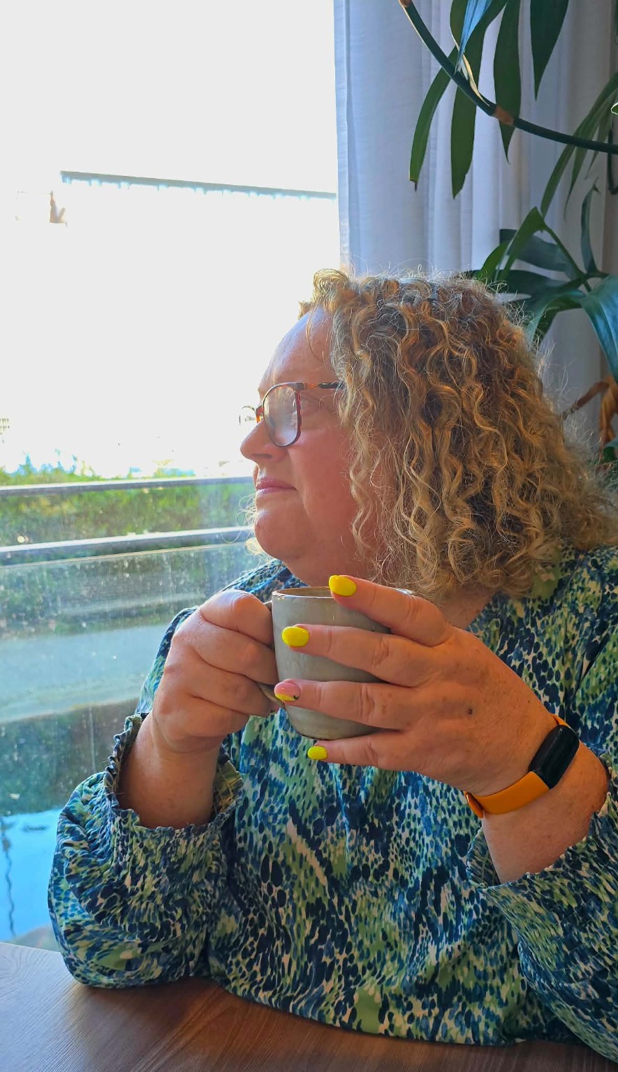 Carol Whiteley sitting thoughtfully with a cup of coffee